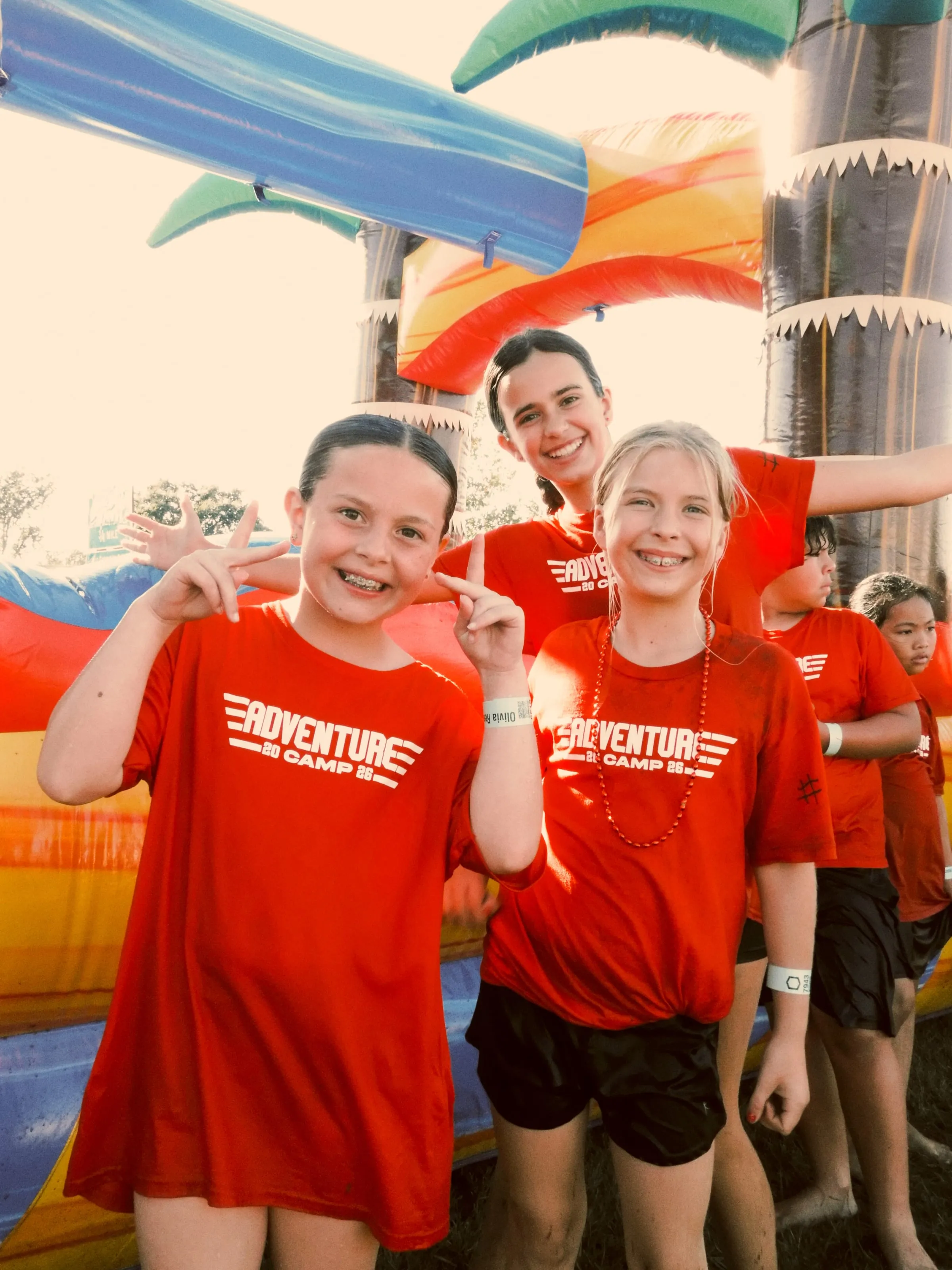 Three campers flash peace signs in front of a tropical inflatable slide.