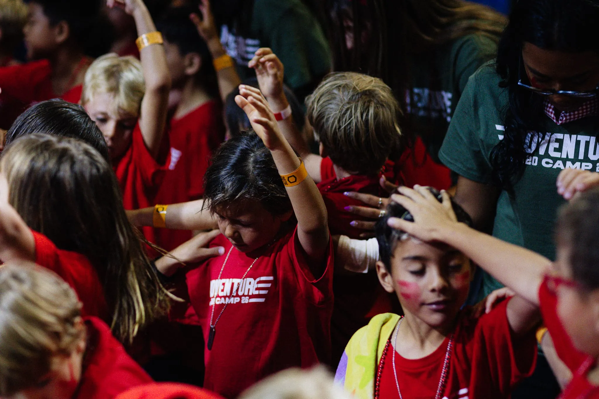 Campers raise their hands together during a worship moment in the auditorium.
