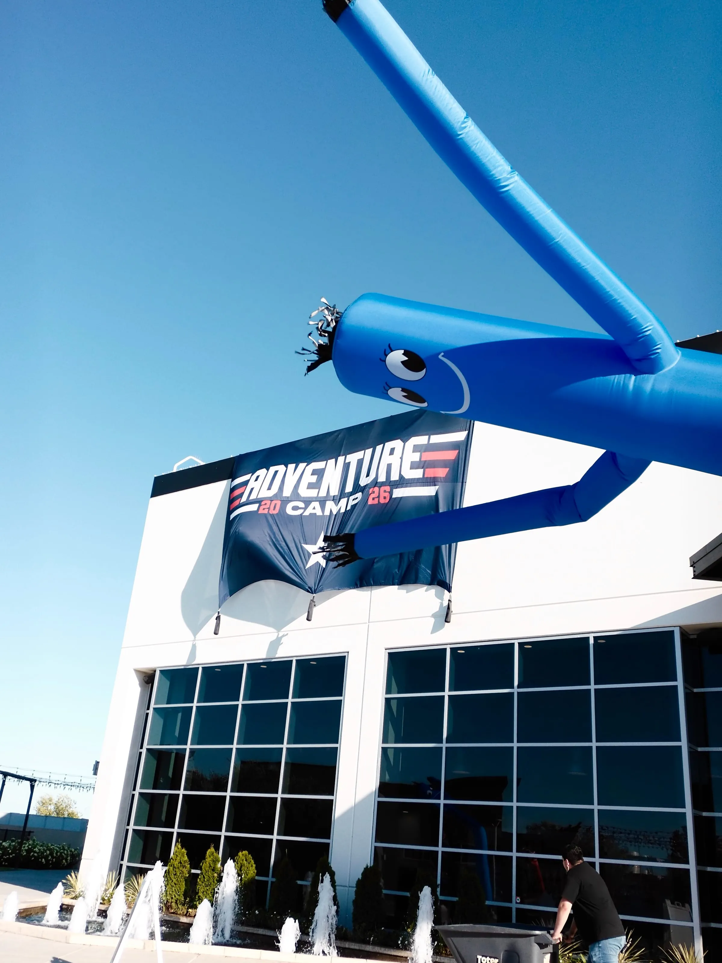 A giant inflatable air dancer waves above the camp building entrance on a sunny afternoon.