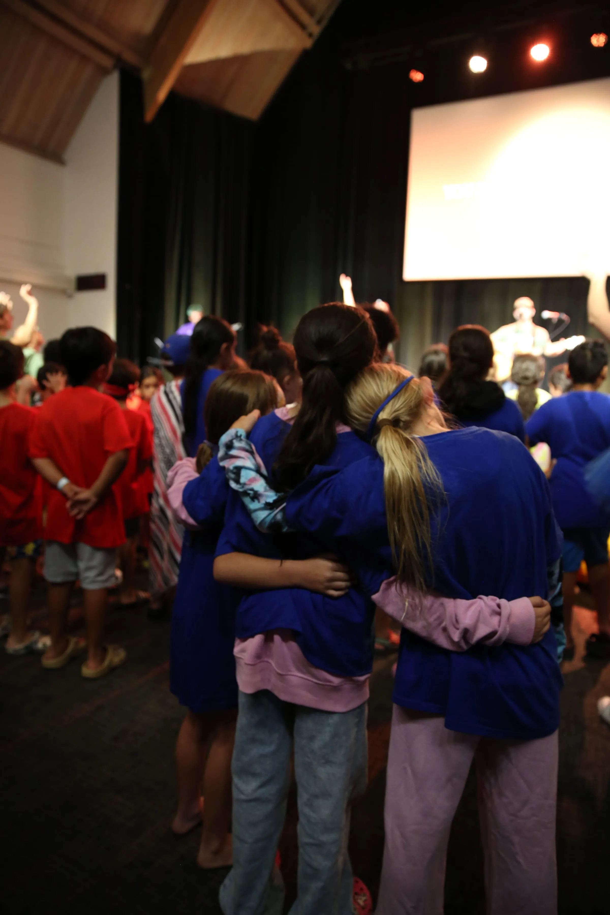 Campers gathered in a dim auditorium, silhouetted against the glow of the stage screen.